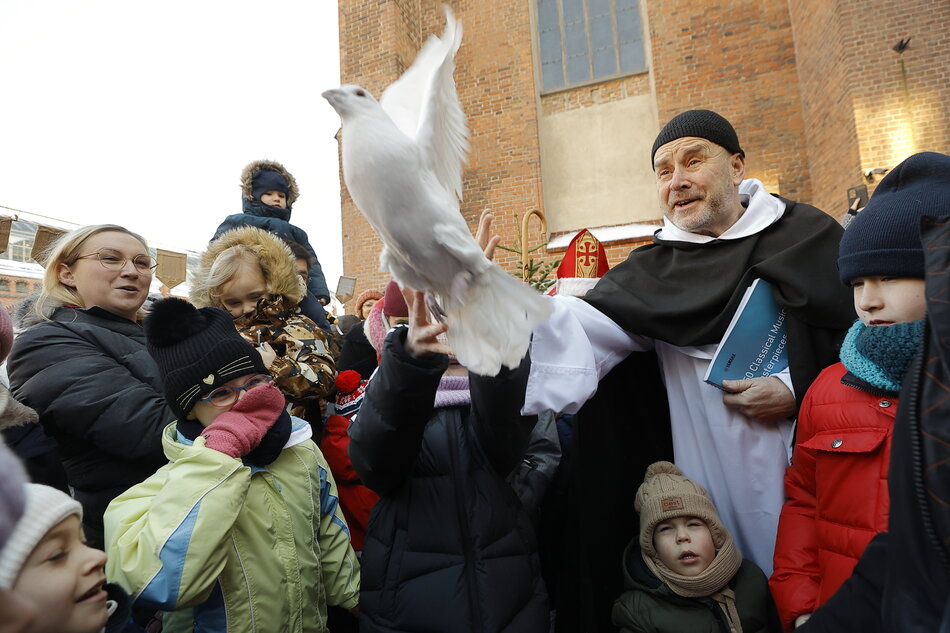 na dziedzińcu zabytkowego kościoła zimą grupa dzieci i zakonnik wypuszczają goęłbia