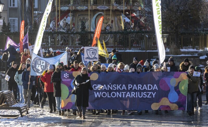parada idąca ulicą, uczestnicy niosą transparent z nazwą Gdańska Parada Wolontariuszy