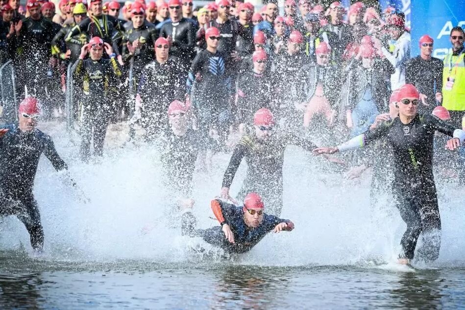pływacy w strojach i czepkach biegną do morza z plaży