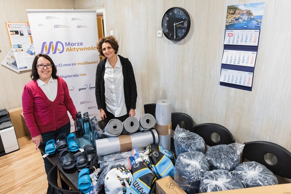 dwie kobiety stoją przy stercie różnego sprzętu turystycznego takiego jak karimaty, bidony i śpiwory