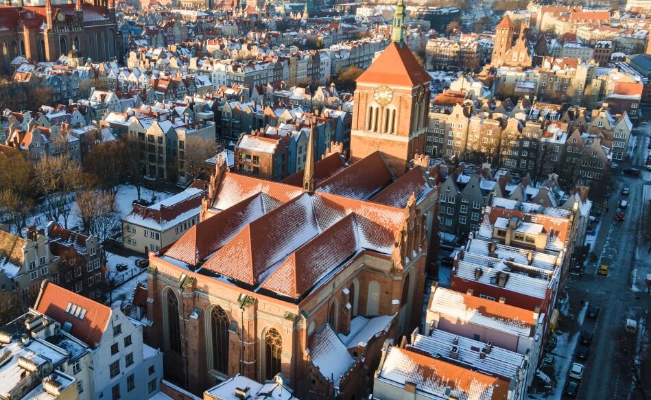 Zabytkowy, ceglany kościół św. Jana w Gdańsku w zimowej scenerii widziany z ltu ptaka, dookoła kamieniczki