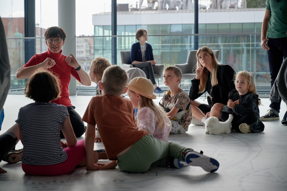 dzieci siedzą na podłodze, przy nich edukatorka