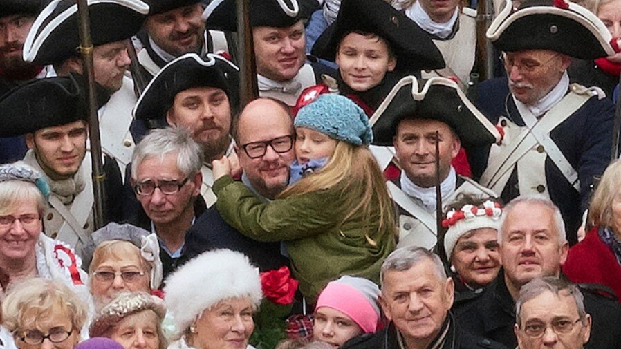 Uśmiechnięty mężczyzna z dzieckiem na ręku, pośród tłumu uczestników gdańskiej Parady Niepodległości 