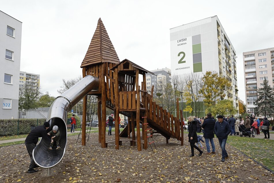na zdjęciu drewniana konstrukcja przypominająca zamek do zabawy dla dzieci, w tle blok mieszkalny i drzewa