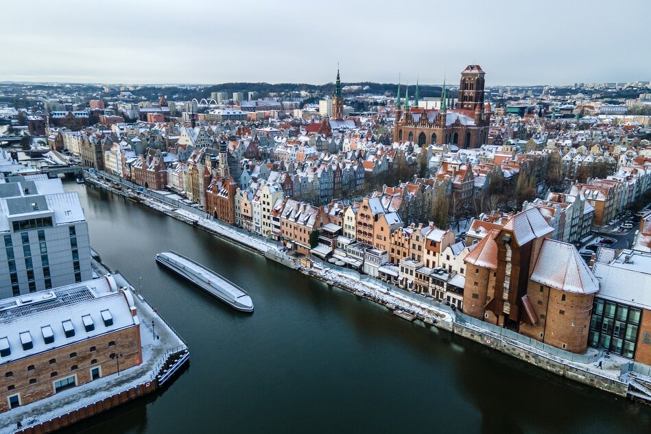 zdjęcie z drona: miasto z rzeką, po której płynie statek. Domy z czerwonymi dachami pokryte są śniegiem