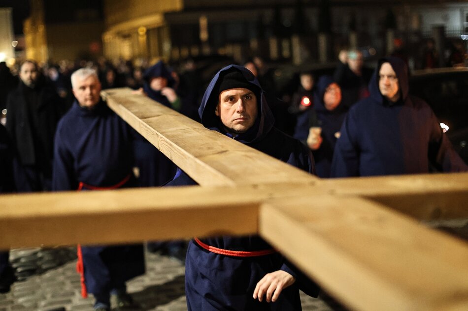 Noc. Na pierwszym planie leżący drewniany kilkumetrowy krzyż niesiony na ramionach kilku mężczyzn. W tle (rozmazani) orszak ludzi 