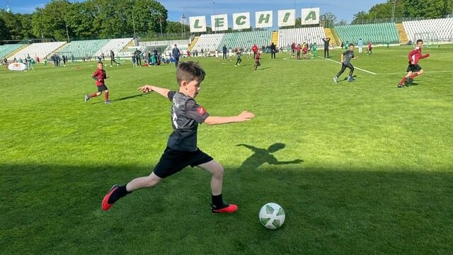 Chłopiec biegnie z piłką, w tle inni młodzi piłkarze