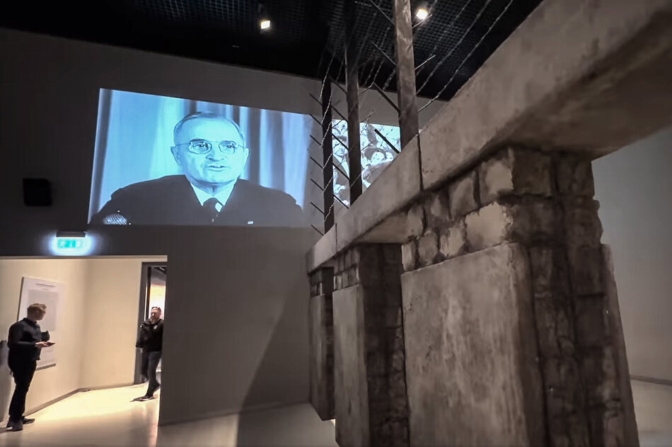 Stop klatka z filmu przedstawia wnętrze Muzeum II Wojny Światowej. Na ekranie wyemitowany jest film dokumentalny. Na ekranie widać twarz prezydenta Stanów Zjednoczonych Harrego Trumana. 
