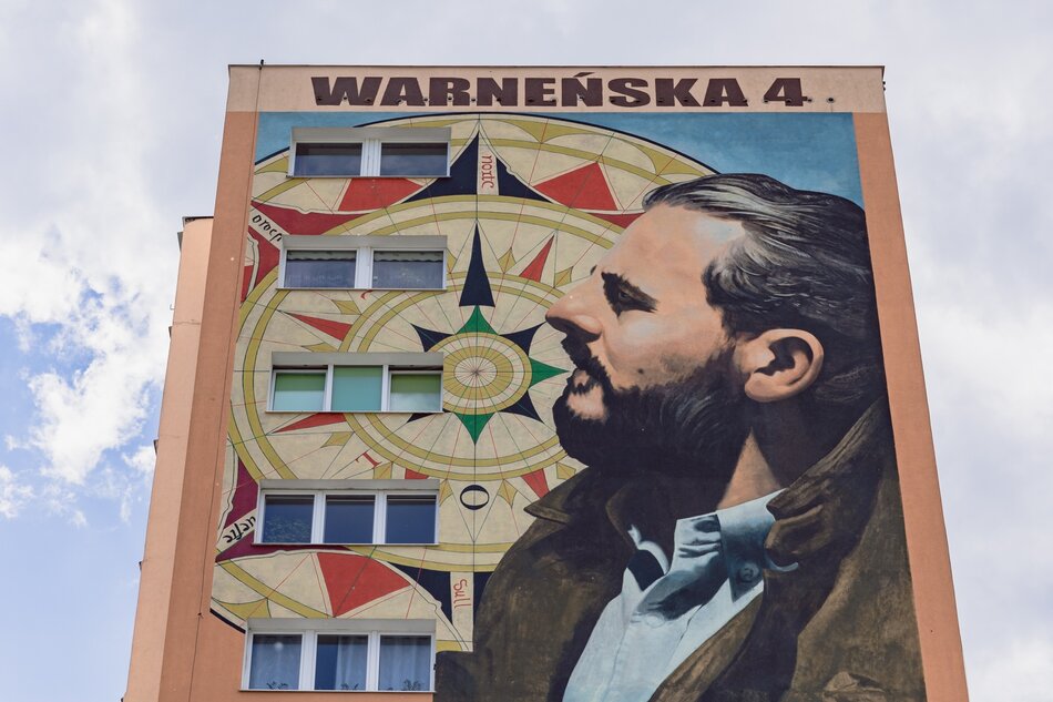 na zdjęciu mural na budynku, przedstawia profil boczny mężczyzny, obok niego namalowana róża wiatrów