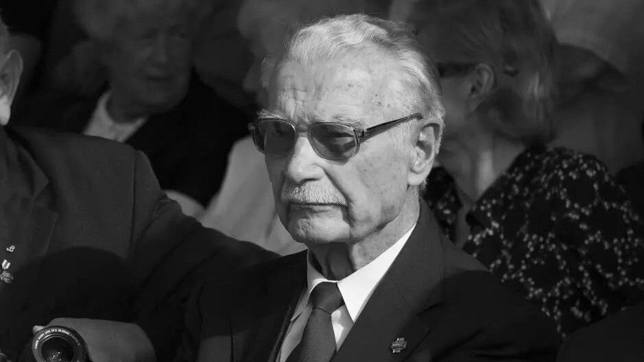 Czarno-białe zdjęcie: mężczyzna w sędziwym wieku, w garniturze, pod krawatem, ma ciemne okulary
