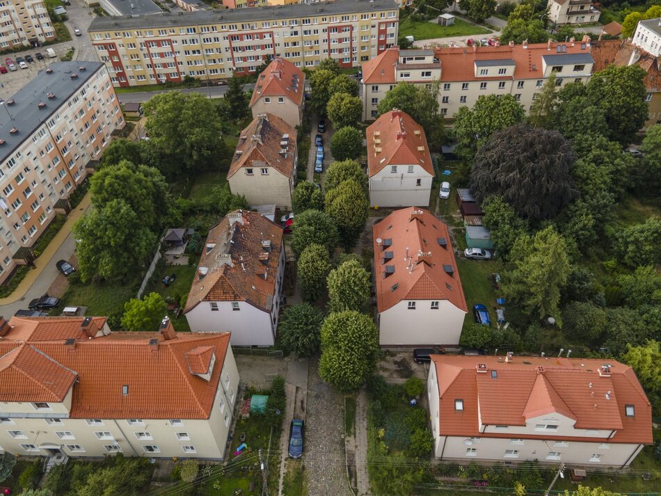 zdjęcie z drona, widać fragment dzielnicy z niewysokimi kamienicami wielorodzinnymi, i prostymi blokami z czasów PRL, wokół budynków niewielkie ulice i mnóstwo zielonych drzew