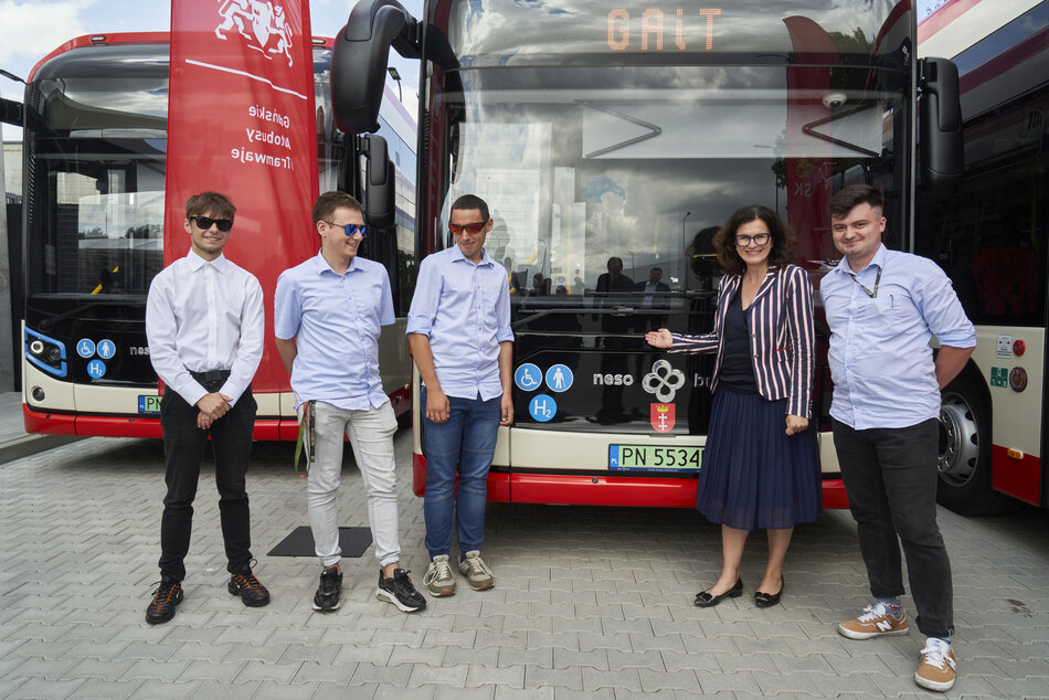 Kobieta i czterech mężczyzn w koszulach pozują do zdjęcia przed nowymi autobusami.