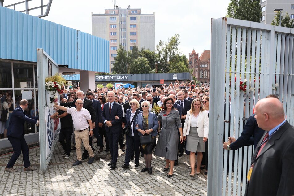 na zdjęciu tłum ludzi, kilka osób otwiera na oścież historyczną bramę stoczniową