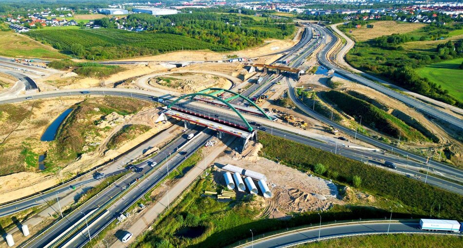 Zdjęcie z lotu ptaka. Węzeł drogowy z wiaduktem. Wokół trwają prace budowlane.