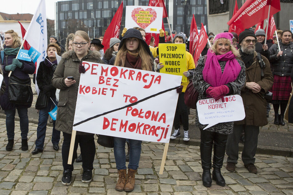 grupa kobiet w różnym wieku stoi na ulicy, trzymają transparenty promujące prawa kobiet.