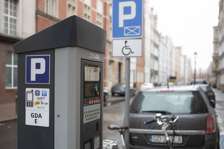 Słupek parkomatu, z ulicą i stojącymi samochodami w tle