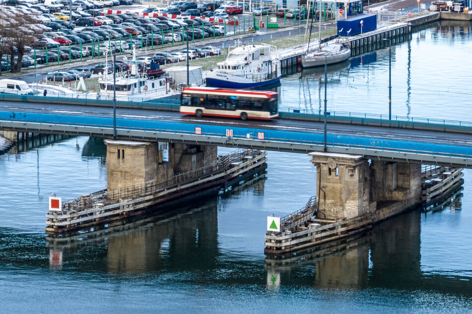 zabytkowy most sfotografowany z lotu ptaka. Pod mostem przepływa rzeka, na moście widoczne przejeżdżające pojazdy. W tle widoczna zabudowa industrialna i zacumowane na brzegu rzeki statki