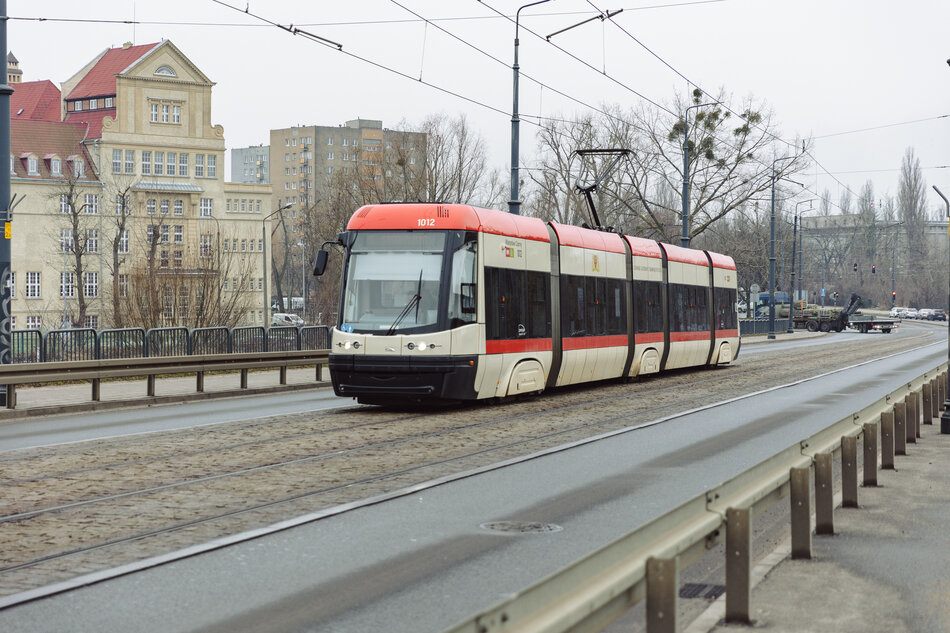 Tramwaj jadący po torach. W tle duży budynek szkoły