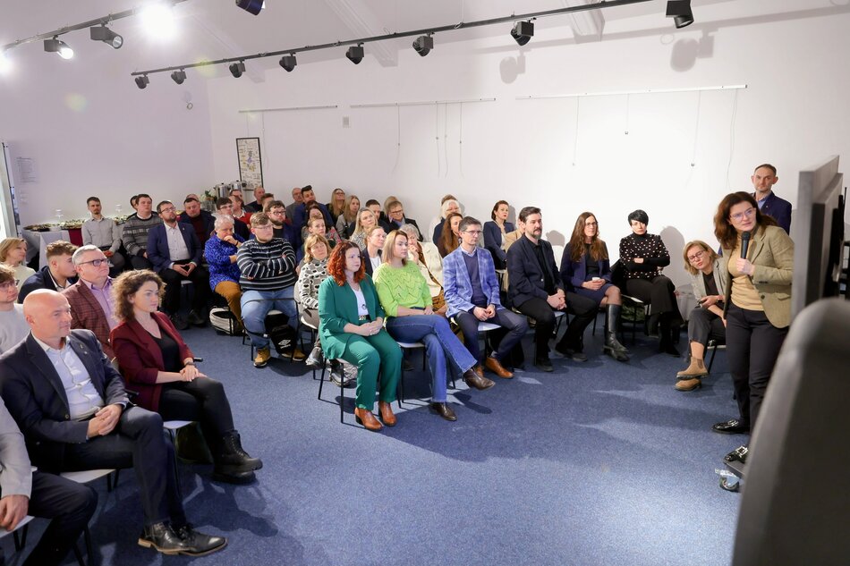 na zdjęciu kilkadziesiąt osób siedzi na krzesłach, w kilku rzędach, w pomieszczeniu o białych ścianach