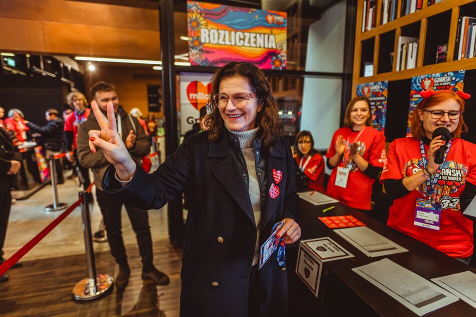 Aleksandra Dulkiewicz w sztabie WOŚP, pozuje do zdjęcia układając palce dłoni w literę V