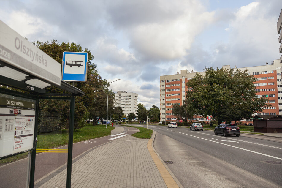 na zdjęciu chodnik i jezdnia, po lewej przystanek autobusowy z wiatą, w tle wysokie budynki mieszkalne