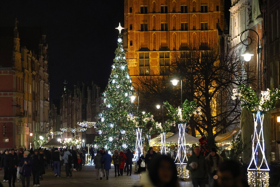 Ulica Długi Targ w Gdańsku wieczorem, zimą, oświetlona świątecznymi iluminacjami. W centrum zdjęcia oświetlona choinka.