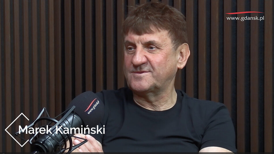 Mężczyzna siedzi przed mikrofonem w studiu nagrań.