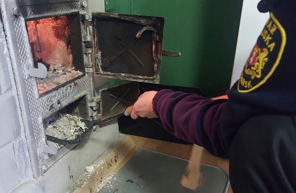 Ręka strażnika miejskiego z szufelką, która sięga do popielnika pieca. 