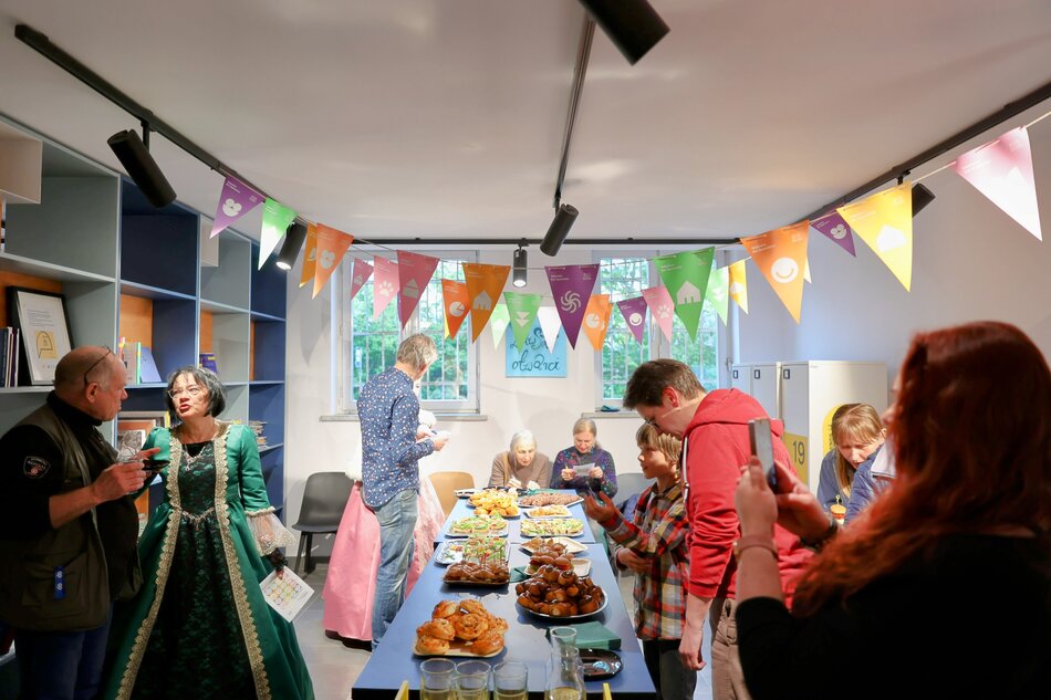 Spotkanie integracyjne w sali, gdzie stoi długi stół, a wokół stoją ludzie.