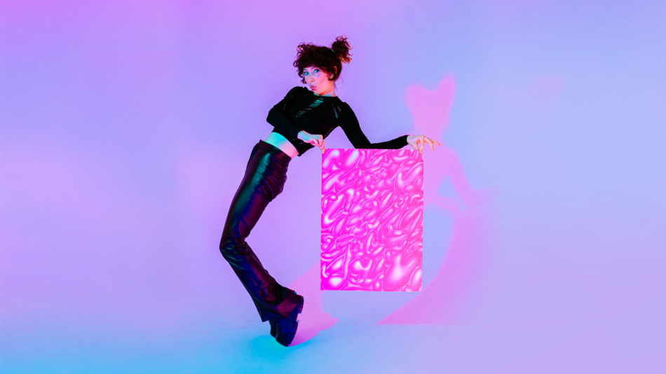 Na zdjęciu wygięta w lewo kobieta ubrana w czarne spodnie i koszulkę, trzymająca w rękach różowo-białe dzieło