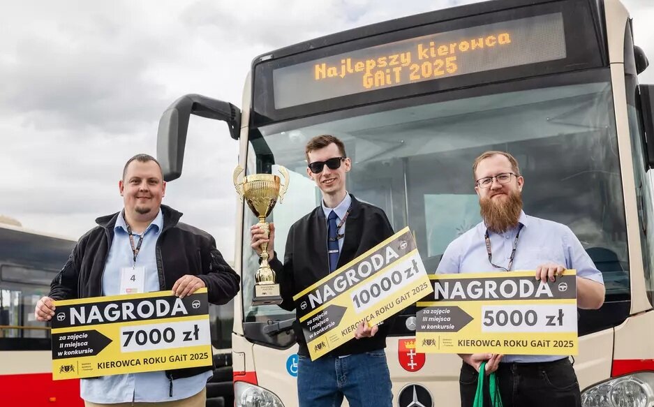 Na zdjęciu trzej zwycięzcy konkursu „Kierowca Roku GAiT 2025” z dumą prezentują swoje nagrody pieniężne oraz puchar, stojąc przed miejskim autobusem z napisem „Najlepszy kierowca GAiT 2025”. Uśmiechnięci i elegancko ubrani laureaci trzymają tablice z informacją o zajętych miejscach i wysokości wygranych: 10 000 zł, 7 000 zł oraz 5 000 zł. 