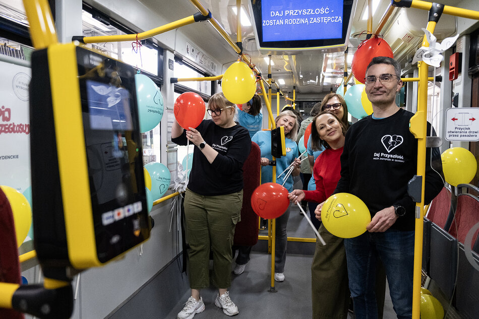 Pracowni Miejskiego Ośrodka Pomocy Rodzinie w Gdańsku pozują uśmiechnięci do zdjęcia w tramwaju ozdobionym balonami podczas akcji informacyjnej o rodzinach zastępczych. 