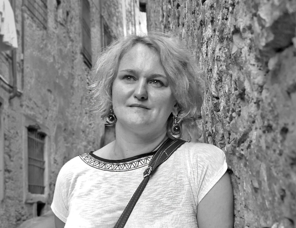 Na czarno-białym zdjęciu kobieta z jasnymi włosami za uszy, ubrana w białą bluzkę.