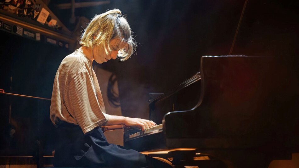 Na zdjęciu kobieta pochylona nad instrumentem klawiszowym.
