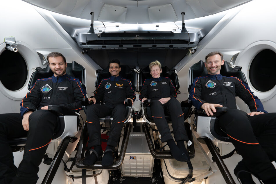Czwórka astronautów na pokładzie rakiety - trzech mężczyzn i jedna kobieta, siedzą na fotelach i uśmiechają się. 