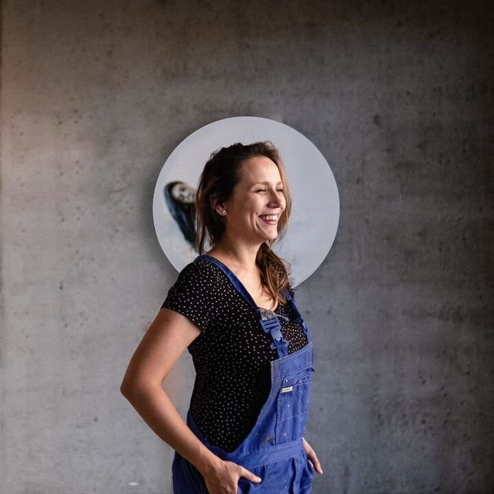 Na zdjęciu kobieta w jeansowych spodniach i czarnej koszulce, w tle praca autorska w kształcie okręgu.