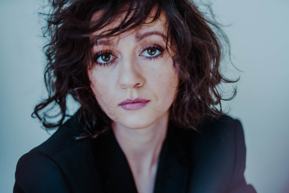 Na zdjęciu kobieta z rozwianymi włosami, na sobie ma ciemną marynarkę.