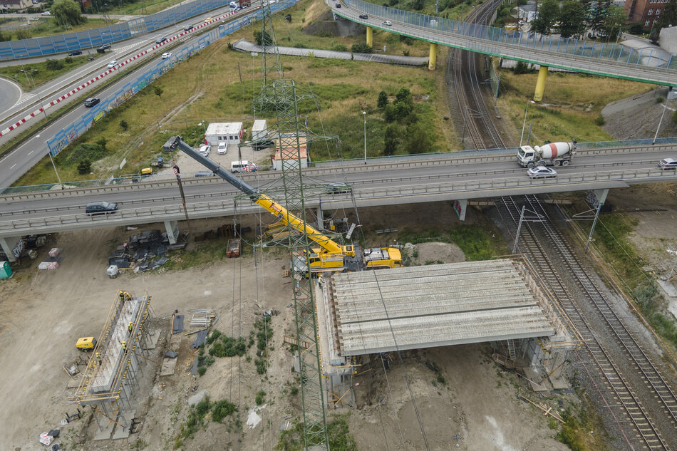 zdjęcie z drona, widać plac budowy, betonowe filary nowej estakady i żółtą koparkę, w tle jezdnie innych estakad