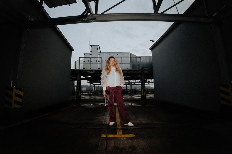 Na zdjęciu kobieta z włosami za ramiona, w tle budynki.