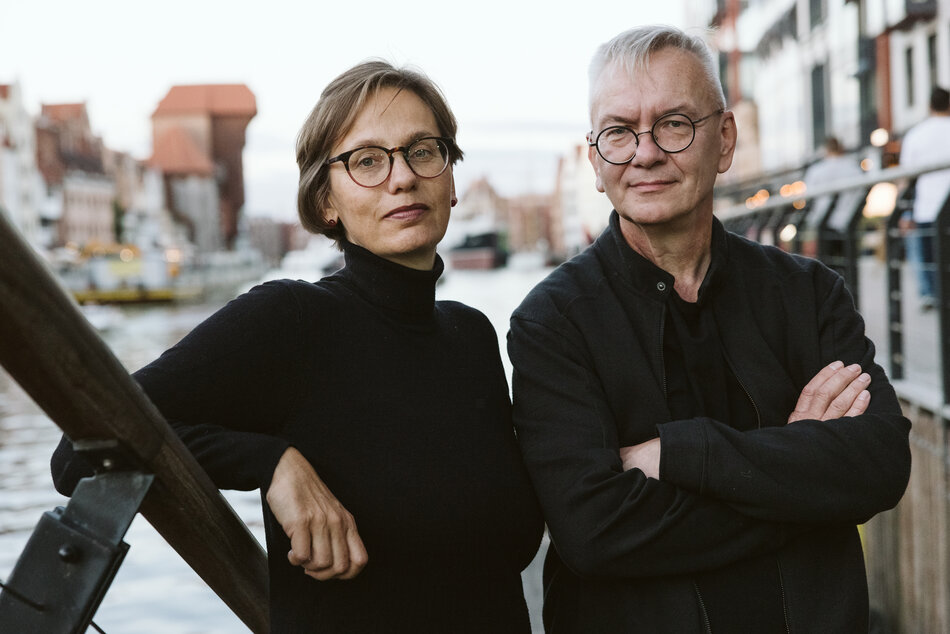 Na zdjęciu kobieta i mężczyzna w czarnych strojach, oboje w okularach, w tle zabytkowe budynki Gdańska.