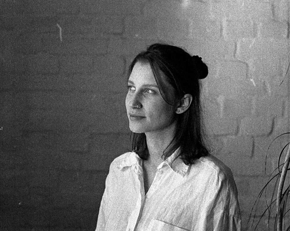 Na zdjęciu kobieta patrząca w lewo, na sobie ma białą koszulę, stoi na tle białej ściany z cegły.