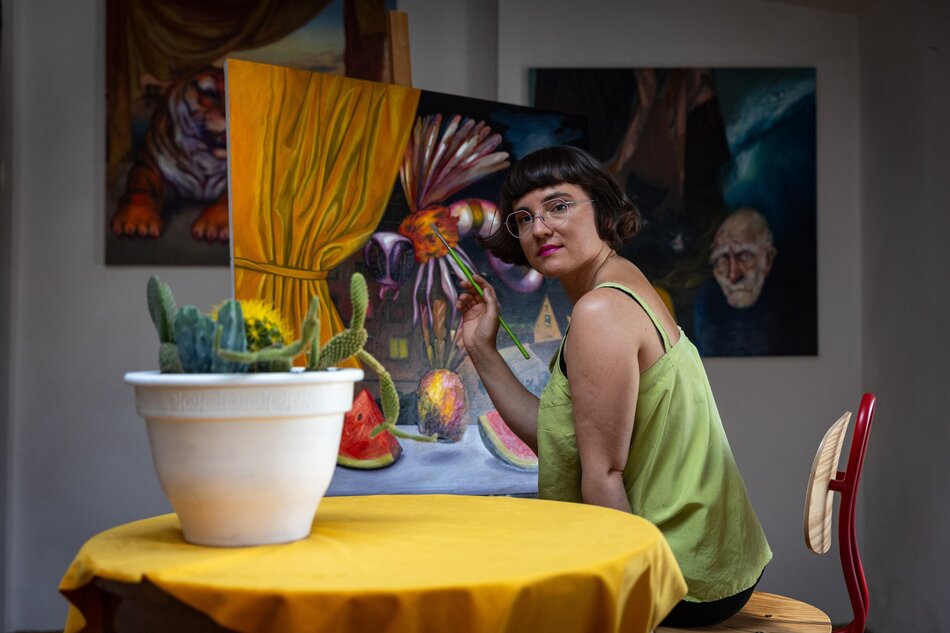 Na zdjęciu kobieta siedząca na krześle, malująca obraz.