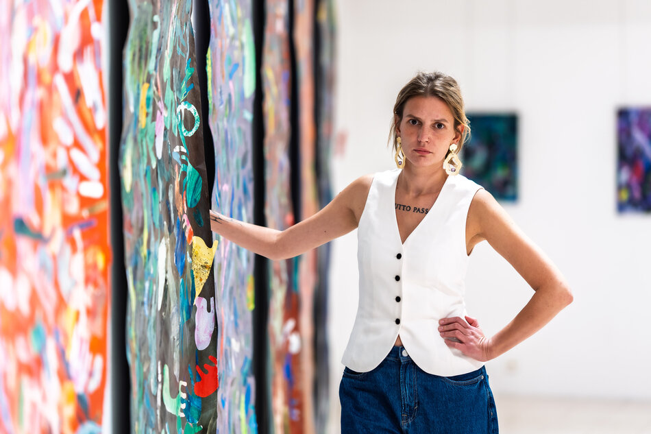 Na zdjęciu młoda kobieta opierająca się o malowane dzieła sztuki.