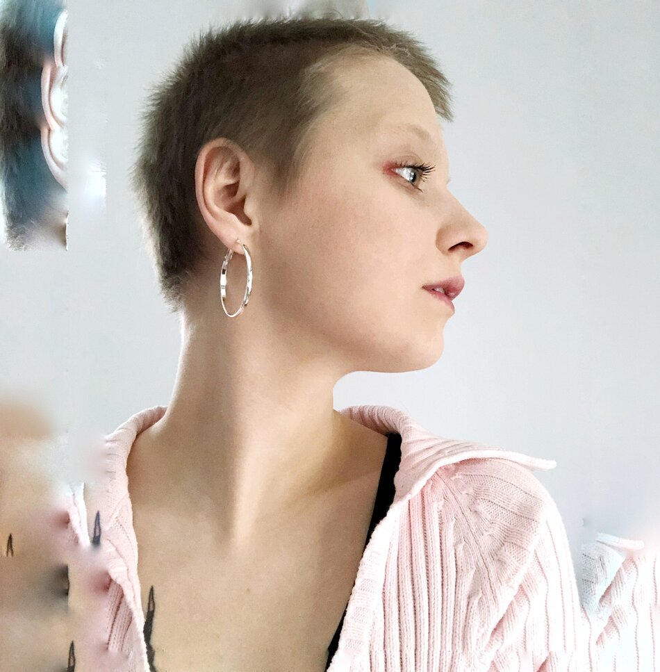 Na zdjęciu profil kobiety o krótkich włosach, z kolczykiem w kształcie okręgu w uchu.