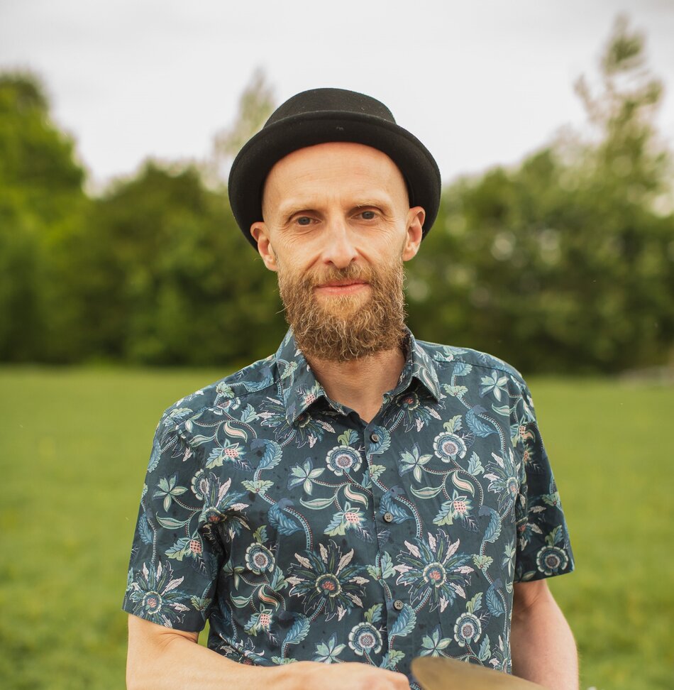 Na zdjęciu mężczyzna w czarnym kapeluszu i koszuli w kwiaty na tle zieleni.