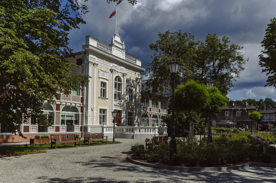 na zdjęciu zabytkowy, dwukondygnacyjny budynek dawnego domu zdrojowego, otoczony zielenią