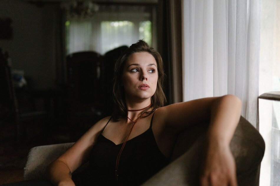 Na zdjęciu młoda kobieta w czarnej koszulce na ramiączkach, siedząca w fotelu.