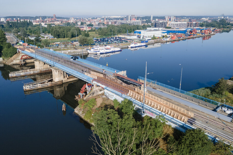 zdjęcie z drona, widać most, nieco rozkopany, pod nim rzeka, w tle tereny stoczniowe