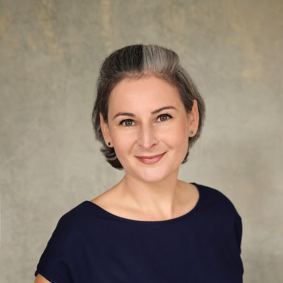 Na zdjęciu kobieta w krótkich włosach, za uszy, w ciemnej koszulce.