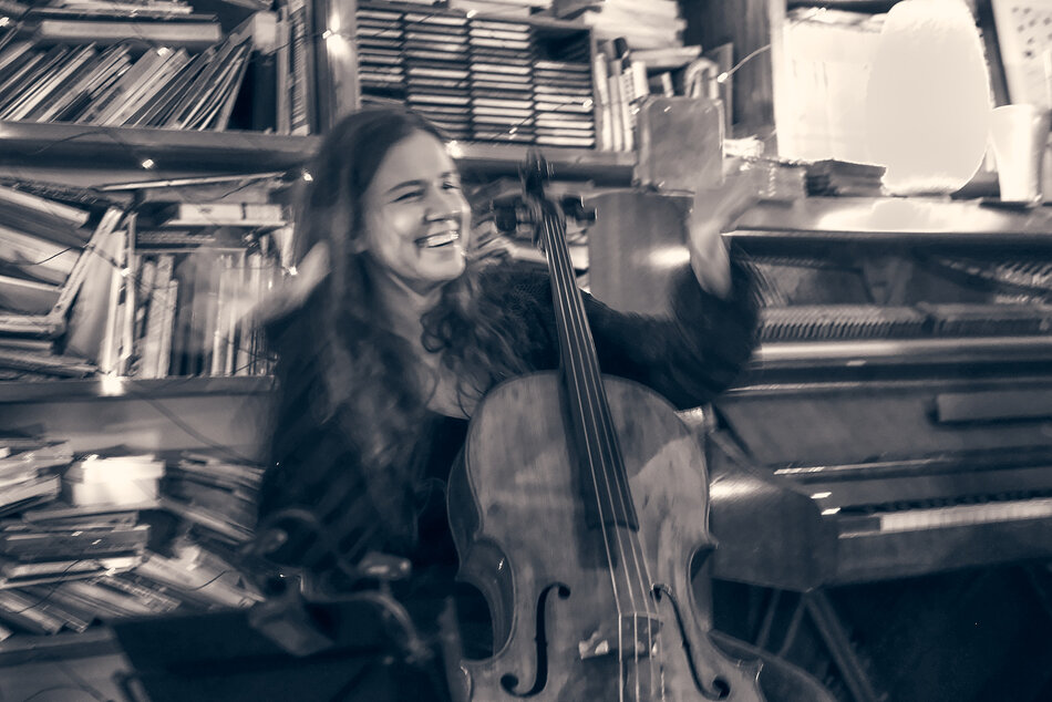 Kobieta z długimi włosami, trzymająca instrument smyczkowy na tle książek.